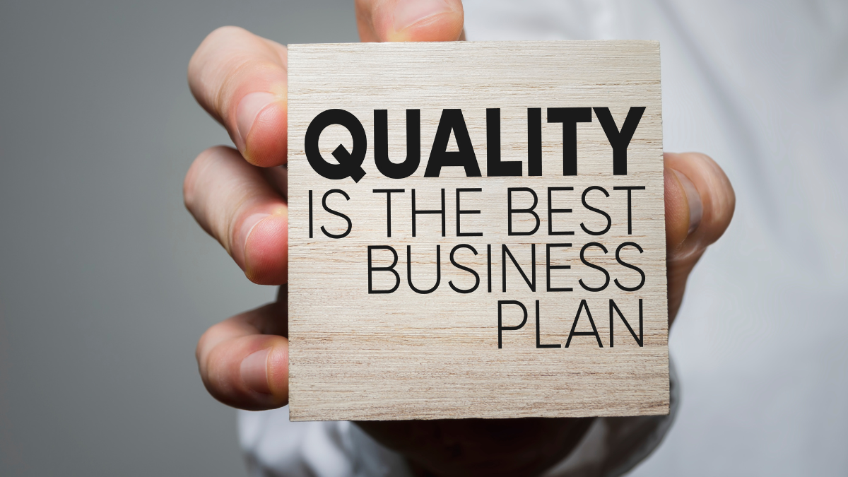 Hand holding a wooden block that reads 'Quality is the best business plan'.