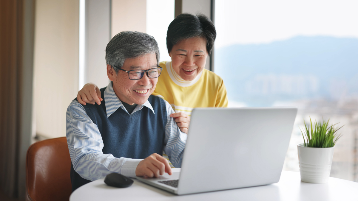 Smiling older couple looking at a laptop together at a table.