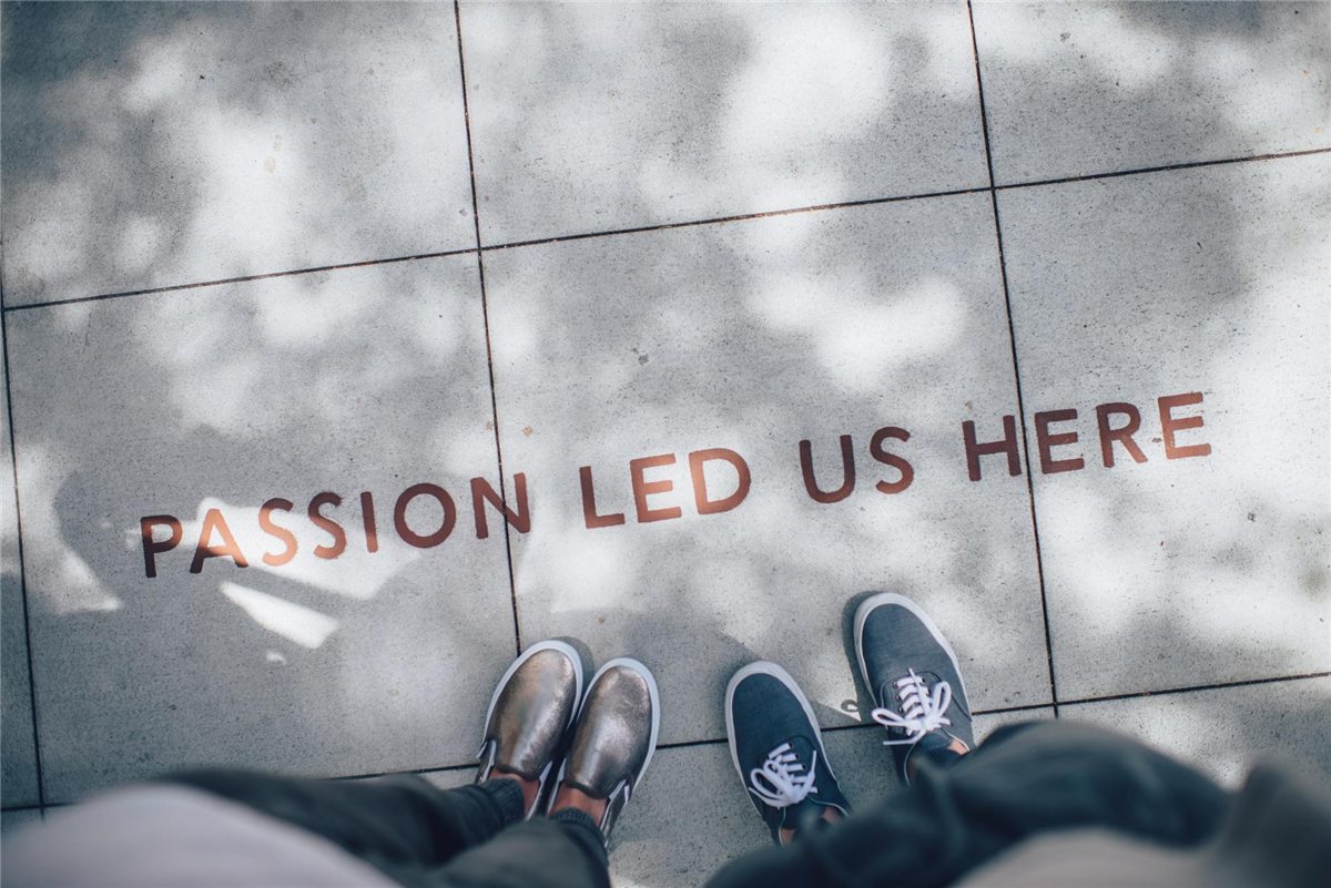 Two pairs of shoes on a pavement printed with the words 'Passion led us here'.